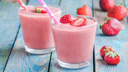 Bild von Erdbeer-Lassi mit Strohhalm auf Holztisch.