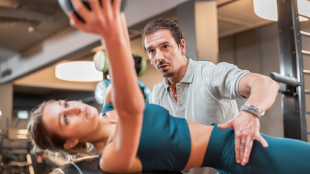 Trainer, der junger Frau bei Übung im Liegen hilft.