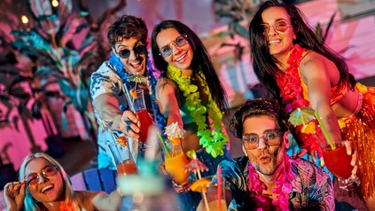 Mehrere junge Leute bei einer Beachparty. Sie tragen Hawaiihemden und Blumenketten um den Hals.
