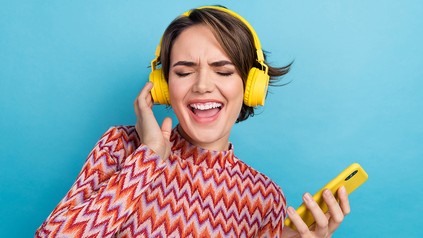 Eine junge Frau hat Kopfhörer auf den Ohren und spielt Musik von ihrem Smartphone ab.