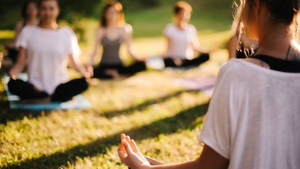 Ein Gruppe von Frauen sitzt auf einer Wiese und macht Yoga.