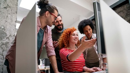 Vier Studierende, die gemeinsam um einen PC stehen und lächeln.