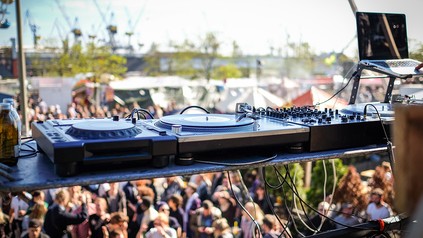 Ein Mischpult und feiernde Partygäste vor der Kulisse des Hamburger Hafens.