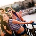 Studierendengruppe, die sommerlich gekleidet auf einer Brücke mit Sicht aufs Wasser ein Selfie macht.