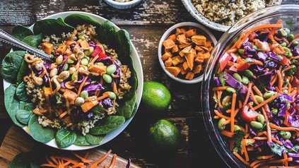 Bowl und Salat in Schüsseln mit anderen Lebensmitteln auf einem Holztisch.