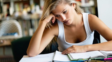 Eine junge Frau sitzt in der Bibliothek und lernt. Vor ihr auf dem Tisch hat sie ihre Lernunterlagen ausgebreitet.