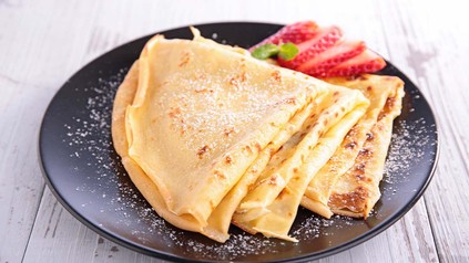 Crepe mit Erdbeeren angerichtet auf einem schwarzen Teller.