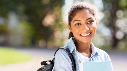 Studentin mit Rucksack und Studienunterlagen lächelnd draußen.