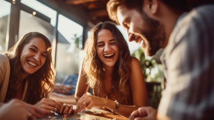 Zwei junge Frauen und ein Mann am Tisch zusammen bei einem Brettspiel.