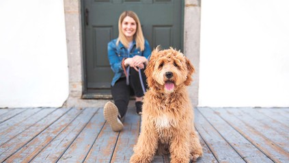 Studentin, die mit ihrem kleinen braunen Hund an der Leine draußen in einem Türrahmen sitzt.