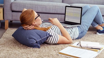 Studentin, die mit dem Laptop auf dem Boden liegt und arbeitet.