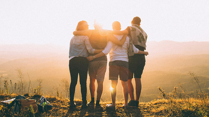 Vier Freunde, die sich an den Schultern halten im Urlaub vor dem Sonnenuntergang.