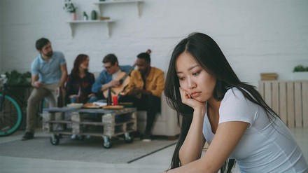 Traurige junge Frau alleine im Vordergrund – im Hintergrund ihre Freund:innen.