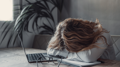 Frau, die ihren Kopf vor dem Laptop auf dem Schreibtisch abgelegt hat, Office.