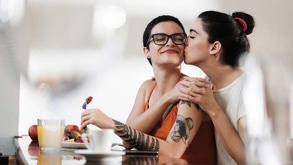 Lesbisches Pärchen, von der eine der anderen morgens einen Kuss auf die Wange gibt.