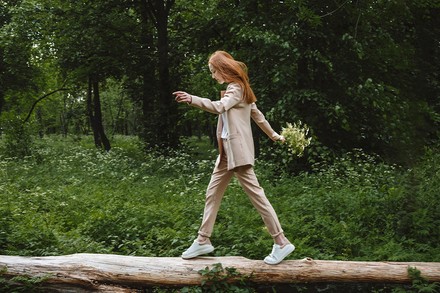 Junge, rothaarige Frau balanciert im Wald auf einem Baumstamm (Foto: © stock.adobe.com/ Irissca)