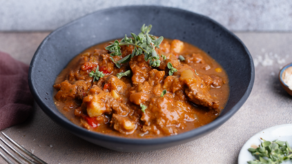 Gulasch in Schüsselchen auf Tisch, drapiert mit Grünzeug.