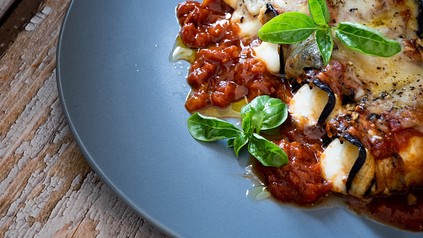 Ein blauer Teller mit Auberginen-Röllchen mit Käse und Tomaten-Sugo