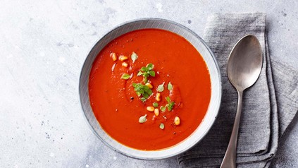 Tomatensuppe angerichtet mit Kräutern und Löffel auf dem Tisch.