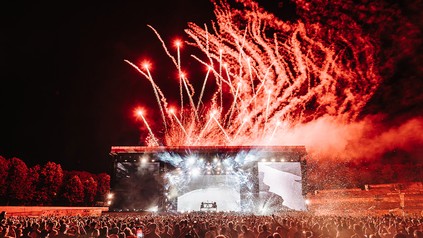 viele Menschen vor einer Bühne, die in rotes Pyro-Licht getaucht ist
