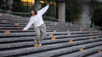 Frau in Jogginghose, die draußen eine Treppe herunter tanzt.