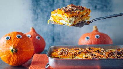 Kürbislasagne in Ofenform auf Tisch, auf dem Hokkaidokürbisse liegen.
