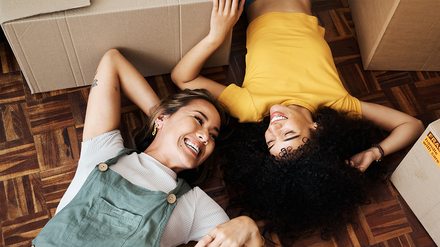 Zwei Freundinnen, die auf dem Boden zwischen Umzugskartons liegen.