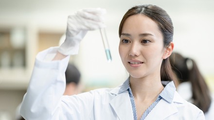 junge, chinesische Frau mit Reagenzglas in der Hand