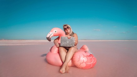 junge Frau sitzt am Meer auf einem aufgeblasenen Flamingo