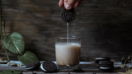 Milchglas mit Hand, die einen Oreo-Keks reintunkt.