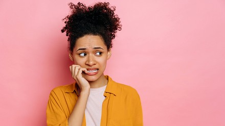 Junge Frau vor pinkfarbenen Hintergrund kaut zweifelnd an ihrem Finger