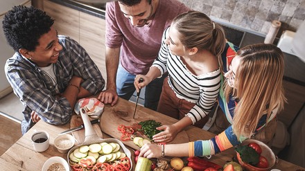 Zwei junge Frauen und zwei junge Männer schneiden zusammen Gemüse in einer Küche