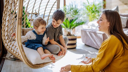 Junge Frau spielt mit zwei kleinen Kindern, die in einem Hängekorb sitzen