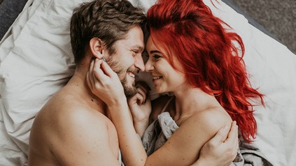 Ein Mann und eine Frau liegen eng aneinander gekuschelt in einem Bett und sind glücklich