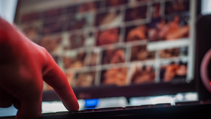 Hand an Tastatur vor verschwommenem Bildschirm mit potenziell ponografischem Inhalt.