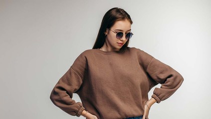 Junge Frau mit dunkelbraunem Sweat-Pullover und Sonnenbrille.