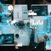 Blick auf einen Arbeitsplatz von oben, mehrere Menschen arbeiten an Pads oder Laptops, das Bild wird überlagert von Grafiken und Tabellen