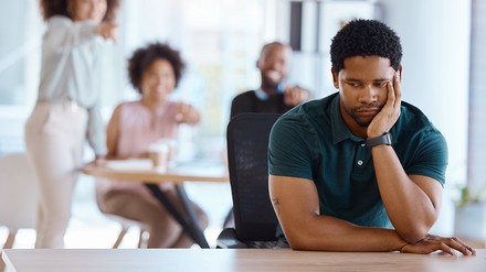 Trauriger junger Mitarbeiter, der von seinen Kolleg:innen ausgegrenzt wird.