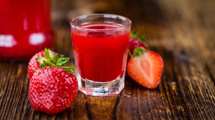 Selbstgemachter Erdbeerlimes im Schnapsglas mit frischen Erdbeeren daneben.