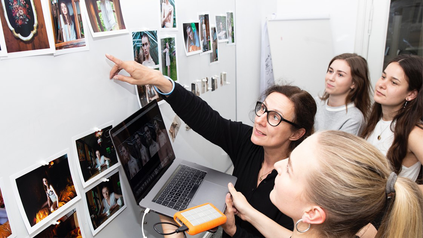 Gruppe Studierender mit Dozentin vor Flipchart-Tafel. Sie diskutieren eine Praxisarbeit.