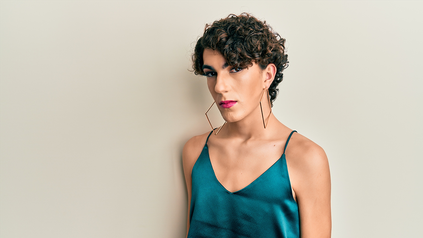 Junger Transgender-Man mit großen Ohrringen in Satin-Top.