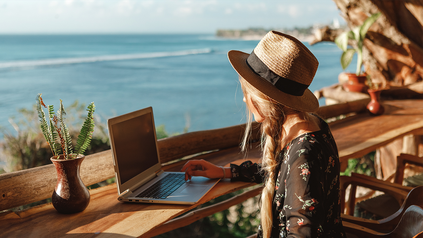 Junge Frau, die mit Sicht aufs Mittelmeer an ihrem Laptop arbeitet.