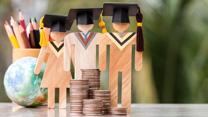Drei Holzfiguren mit Absolventenhut, davor Geld, dahinter eine Weltkugel und Stifte