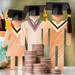 Drei Holzfiguren mit Absolventenhut, davor Geld, dahinter eine Weltkugel und Stifte
