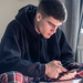 Junger Mann, der im Schneidersitz in seinem Bett sitzt, Smartphone in der Hand, Laptop vor sich.