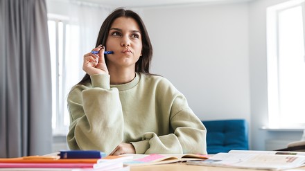 Studentin sitzt am Tisch, auf dem Hefte zur Recherche liegen.
