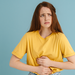 Junge Frau vor hellblauem Hintergrund, die sich mit schmerzverzerrtem Gesicht den Bauch hält.