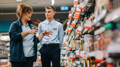 Junge Frau und junger Mann in Angestellten-Outfits in einem Fachhandel vor Regalen.