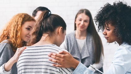 Fünf junge Erwachsene sitzen im Stuhlkreis. Zwei muntern eine andere auf.