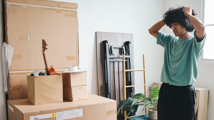 Junger Mann steht verzweifelt zwischen Umzugskartons